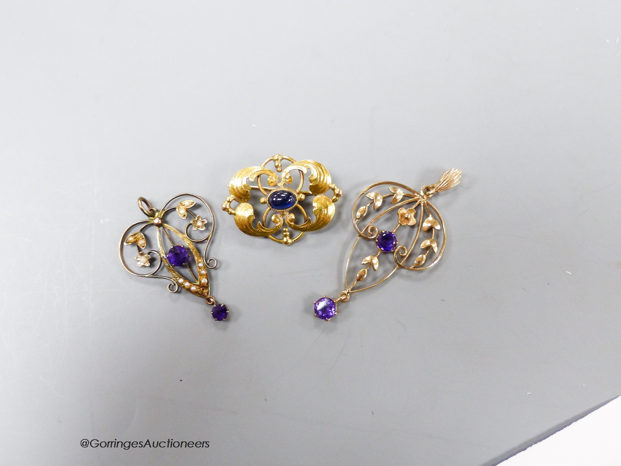 Two early 20th century yellow metal and amethyst set drop pendants, one stamped 9ct with seed pearls, largest 38mm, gross 3.7 grams and a 585 yellow metal and cabochon sapphire set brooch, gross 3.3 grams.